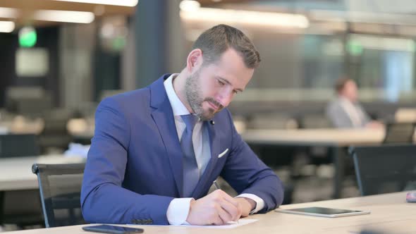 Pensive Middle Aged Businessman Writing on Paper Thinking