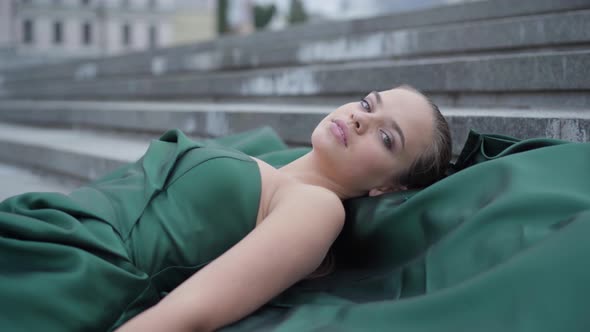 Portrait Cute Young Girl in a Stunning Evening Green Dress Lying on Stairs on Empty City Square Near