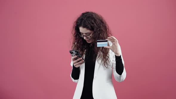 Mature Young Woman with Curly Hair Shopping Online with the Phone Enters the Number on the Card