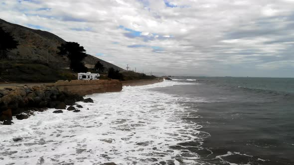 Aerial drone shot on a cloudy day over the Pacific Ocean waves next to RV campers and the cliffs alo