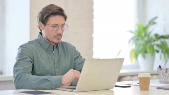 Middle Aged Man Thinking While Using Laptop in Office