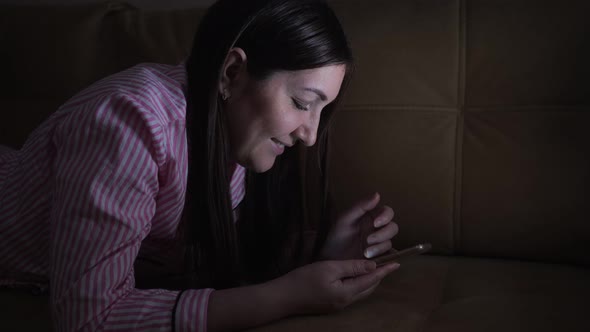 Young Woman Leafing Through a Social Network Feed in the Phone at Night