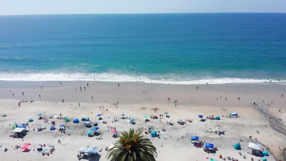 Aerial shot panning across a busy and crowded sandy beach in California, USA