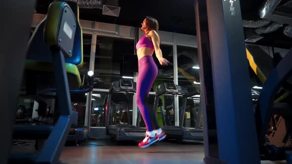 Side view of a full-length woman in sportswear jumping on a rope in gym.