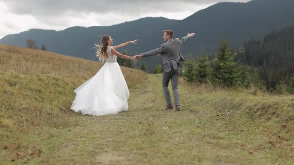 Lovely Young Newlyweds Bride Groom Running on Mountain Slope Holding Hands Wedding Couple Family