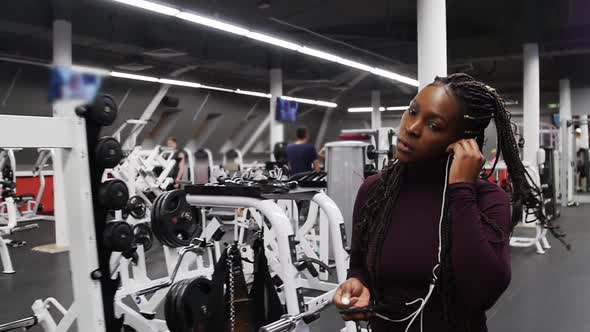 Sports Training  Black Woman Walks in the Gym and Puts on Her Headphones