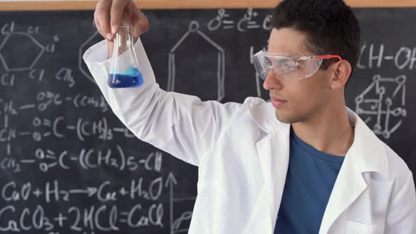 Arabic Chemist Conducting Experiment Mixing Liquids in Flask Laboratory Assistant in Goggles Showing alt