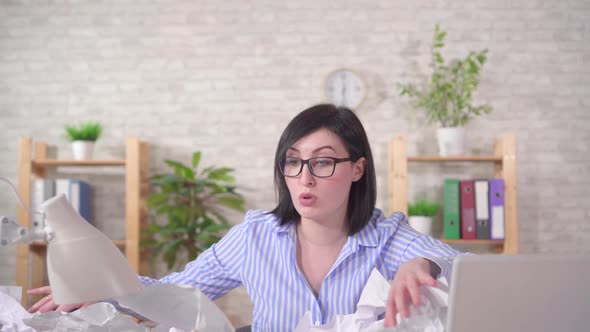 Puzzled Young Woman Office Worker and a Heaps of Papers on the Office Desk