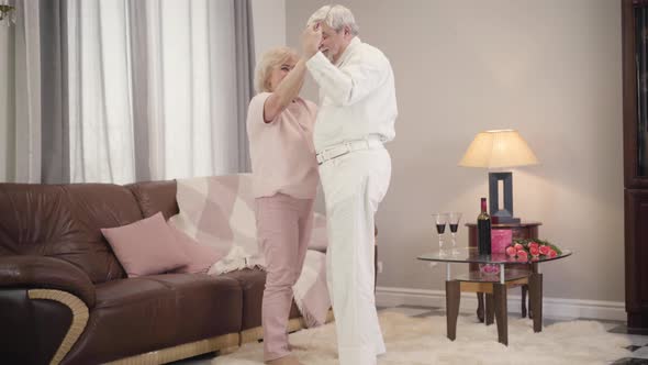 Romantic Dance of Happy Mature Caucasian Couple Indoors, Cheerful Husband Spinning His Lovely Wife