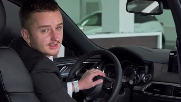 Bearded Businessman Holding Out Car Key To the Camera, Sitting in New Automobile