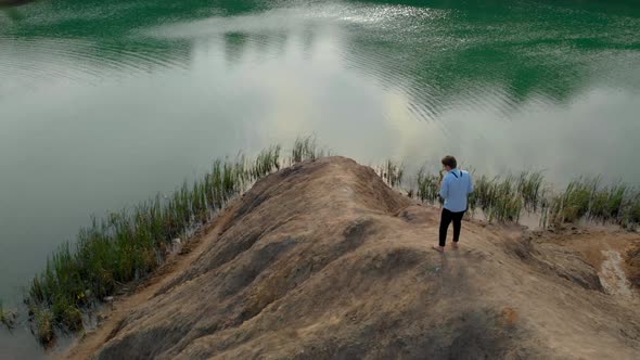 The Musician Plays the Saxophone Standing on the Mountains and Rocks Near the Reservoir. Aerial View