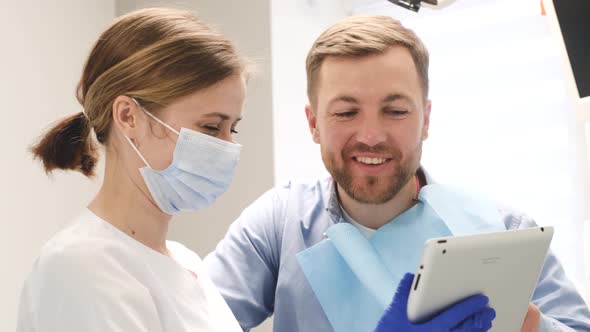 Female Orthodontist Advises a Young Man in the Dental Office a Doctor Holding a Tablet