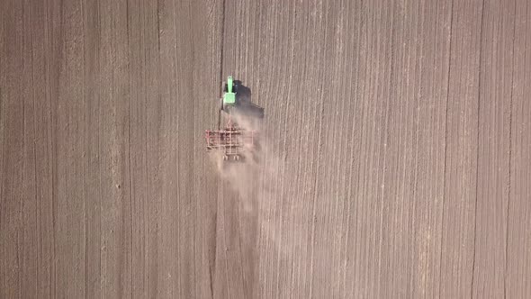 Top down aerial view of green tractor cultivating ground and seeding a dry field. Farmer preparing