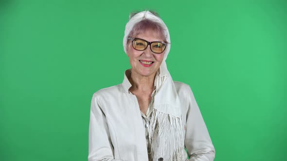 Portrait of Old Stylish Woman Is Looking Straight and Smiling Isolated Over Green Background.