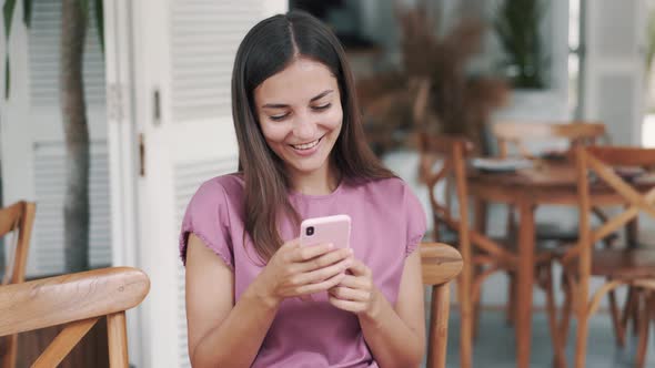 Portrait of Happy Woman Sitting in Cafe and Using Mobile Phone, Laughing