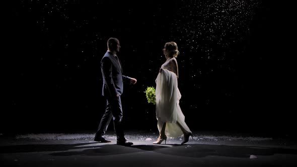 Happy Newlywed Couple Approach Each Other Against the Background of Falling Snow. A Man in a Suit