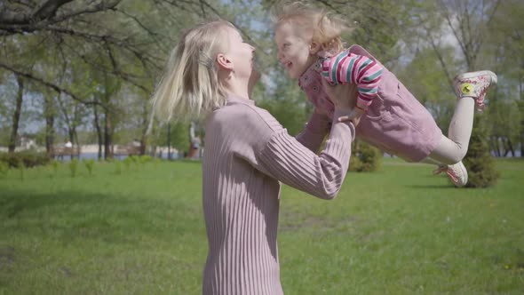 Portrait Cute Young Mother Spinning the Daughter on Hands on Nature on Spring Day. Woman and Kid