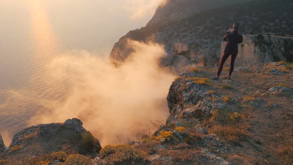 Sporty Young Woman Videotapes Various Fumes and Smoke Coming From Clouds Under a High Mountain