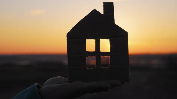 Silhouette Hand with Paper House at Sunset Background