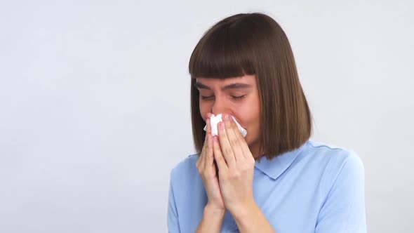 Pretty Young Lady Hardly Sneezing Her Nose Into Tissue in Blue Shirt on Grey Background