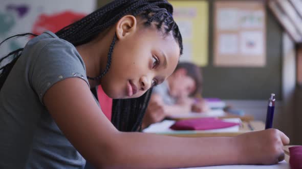 Girl writing in a book while sitting on her desk at school