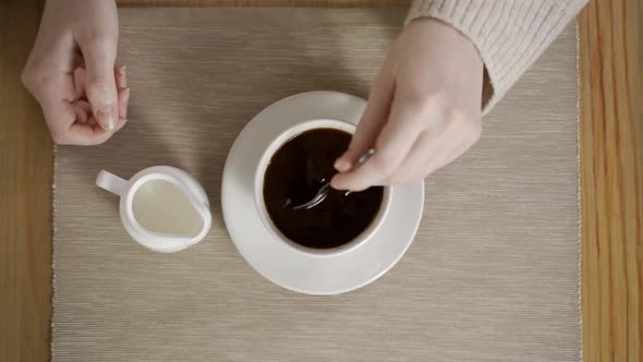 A Woman's Hand Is Stirring Americano and a Creamer Is Standing Nearby