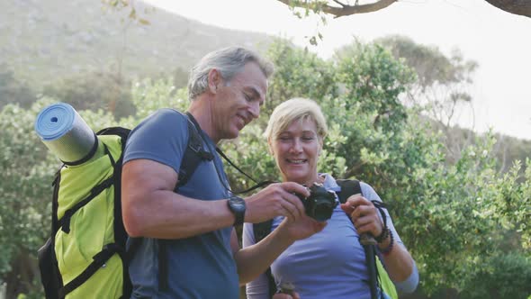 Senior hiking couple with bag packs using digital camera in the woods while hiking in the mountains.