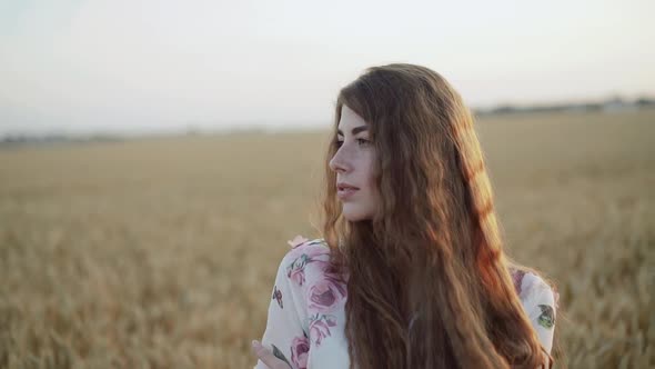 Portrait of Thoughtful Young Lady Embraces Herself and Looks at Camera in Field