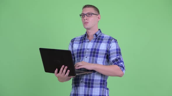 Happy Young Hipster Man Thinking While Using Laptop