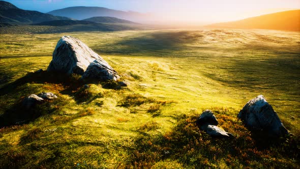 Meadow with Huge Stones Among the Grass on the Hillside at Sunset