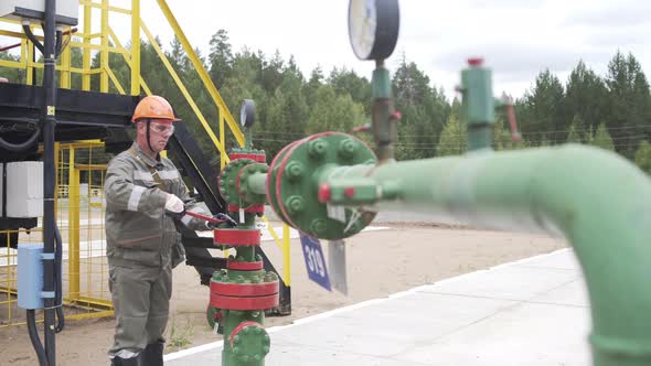 Oilman in Orange Helmet and Protective Glass Opening or Closing Valve of Wellhead. Injection Tree Is