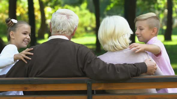 Little Boy and Girl Coming to Grandparents Sitting on Bench in Park, Family Day