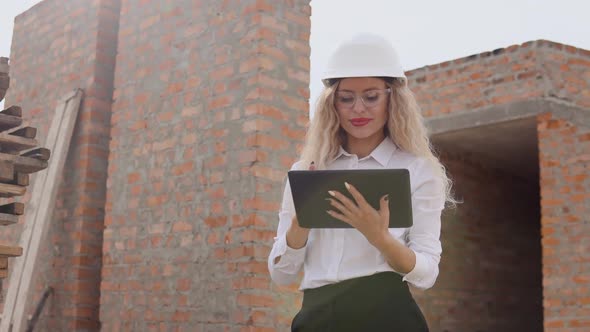 Female Architect in Business Attire and a White Helmet Stands in a Newly Built House with Untreated
