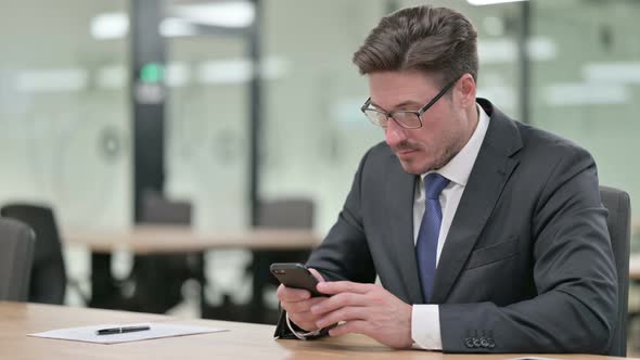 Attractive Middle Aged Businessman Using Smartphone in Office