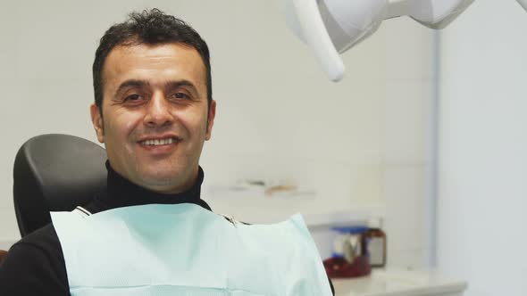 Happy Mature Man Smiling Holding an Apple Sitting in a Dental Chair