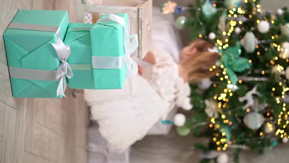 Little Girl Builds a Tower of Gift Boxes Under the Christmas Tree and She Falls