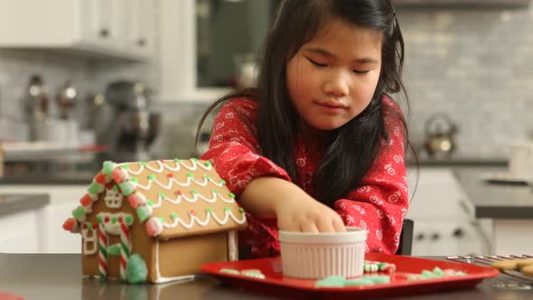 Young girl decorating gingerbread house for Christmas alt