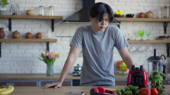 Portrait of Young Asian Man Standing in Kitchen Looking at Healthful Vegetables on Countertop