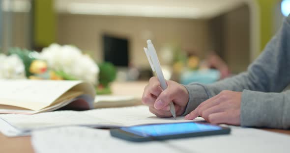 Woman study the note on paper with mobile phone at library 