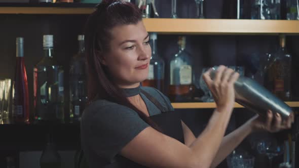 Female bartender shaking craft cocktail in bespoke speakeasy bar.