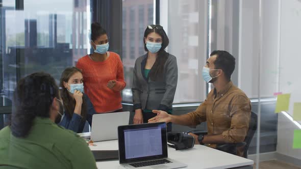 Diverse group of work colleagues wearing face masks discussing in meeting room