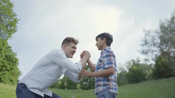 Young Father and the Boy High Five and Shaking Hands Outdoors. Father and a Kid Having Fun in the