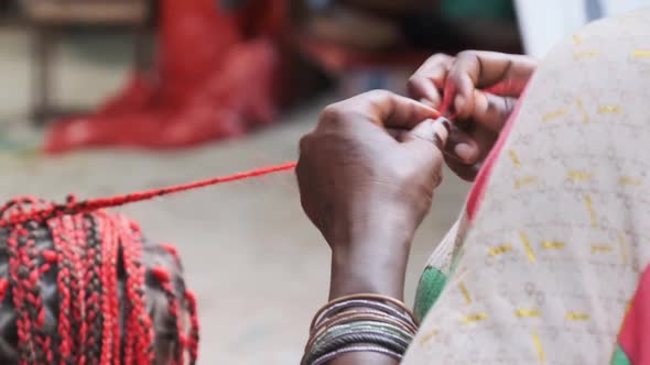 African Woman Weaving African Braids with Red Kanekalon Outdoor Zanzibar Africa