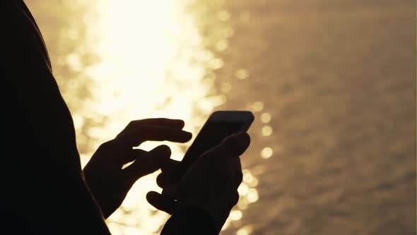 Man Using Cellphone Outdoors Against a Background of Flare Sunlight at Sunset - Closeup.