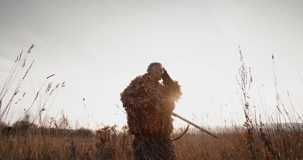 Hunter in Hunting Equipment with Gun Relaxing, Tugs a Hat in the Field Foggy Morning Sunrise Light