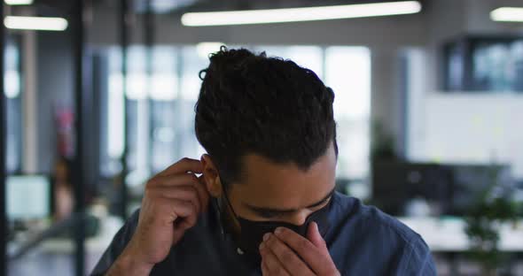 Portrait of mixed race businessman adjusting face mask standing in office and looking to camera