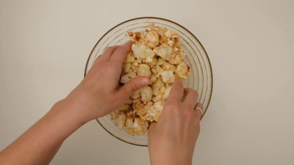 Top view of woman hands mixes cauliflower with paprika and olive oil in bowl