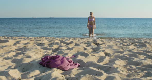 Beautiful blonde woman in a bikini walks out of the water onto the beach on a windy day