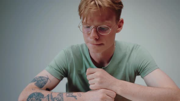 Young Man in Glasses Reading a Textbook and Stressing with His Fist in His Chin