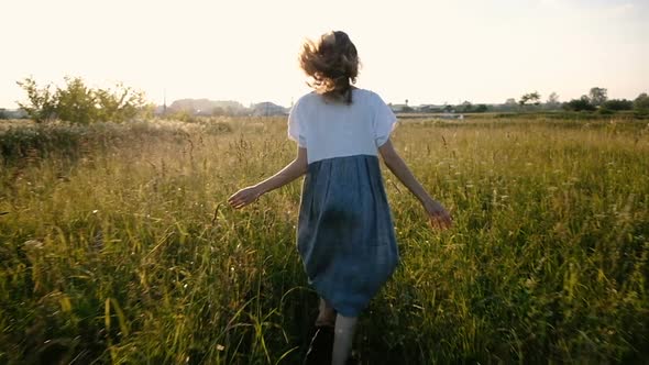 Woman in a Dress Romantically Runs Across the Field with Tall Grass at Sunset